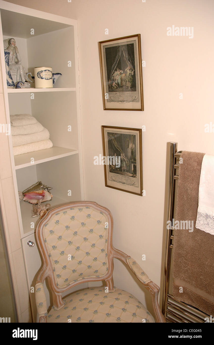 Chaise de style français en face d'étagères blanches au coin d'une salle de bains privative avec gravures encadrées sur le mur Banque D'Images