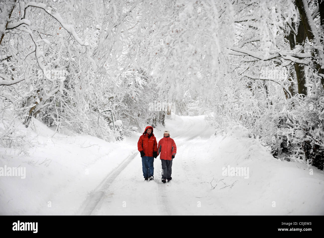 Un couple de manteaux d'hiver rouge correspondant à marcher en voie de Cotswold par temps neigeux UK Banque D'Images