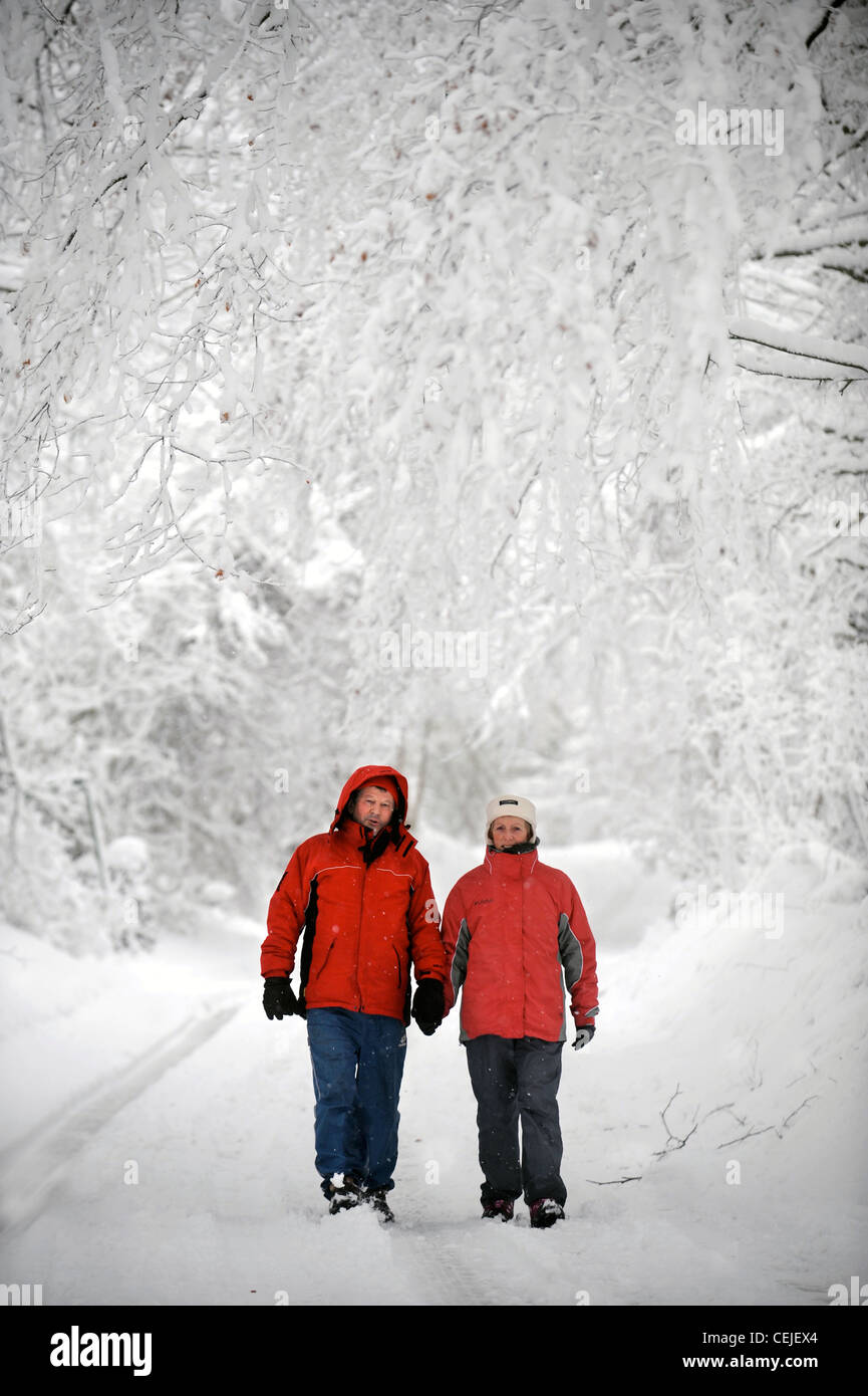 Un couple de manteaux d'hiver rouge correspondant à marcher en voie de Cotswold par temps neigeux UK Banque D'Images