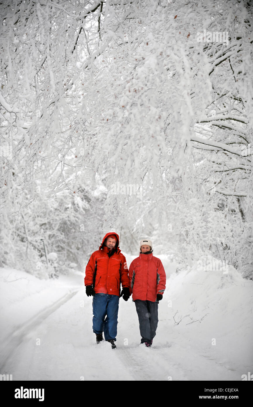 Un couple de manteaux d'hiver rouge correspondant à marcher en voie de Cotswold par temps neigeux UK Banque D'Images