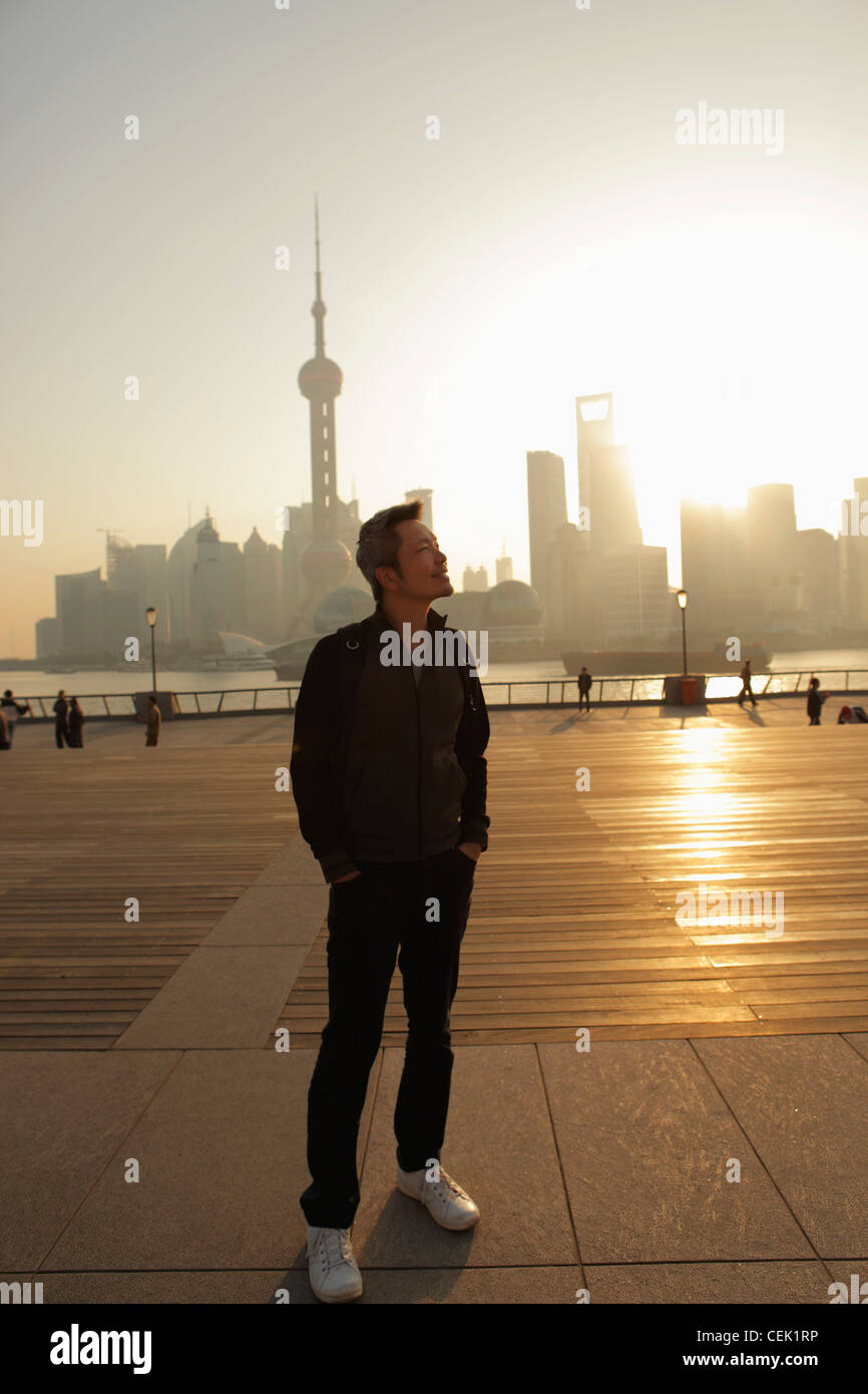 Young man standing in front of city skyline au lever du soleil et sourire, Shanghai, Chine Banque D'Images