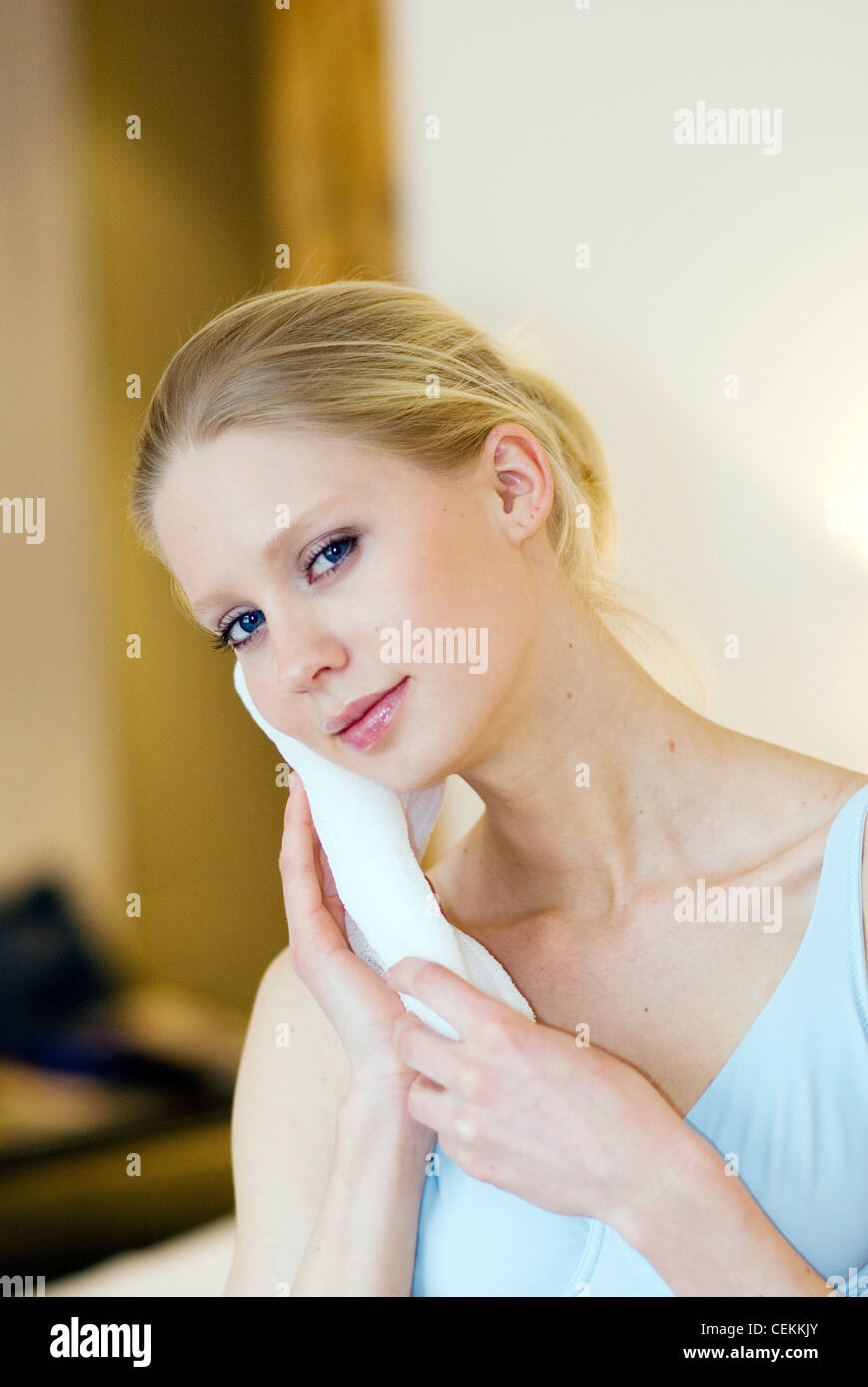 Femme aux cheveux blonds holding chiffon contre joue à la tête penchée sur le côté pour sourire de l'appareil photo Banque D'Images