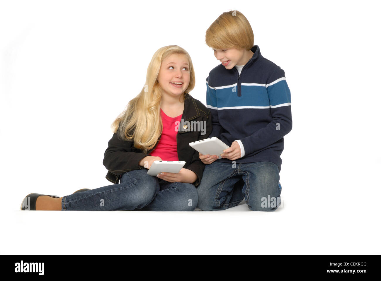 Dix ans, fille et garçon de onze ans à l'aide d'ordinateurs tablettes ou lecteurs de livres électroniques et de sourire. Banque D'Images