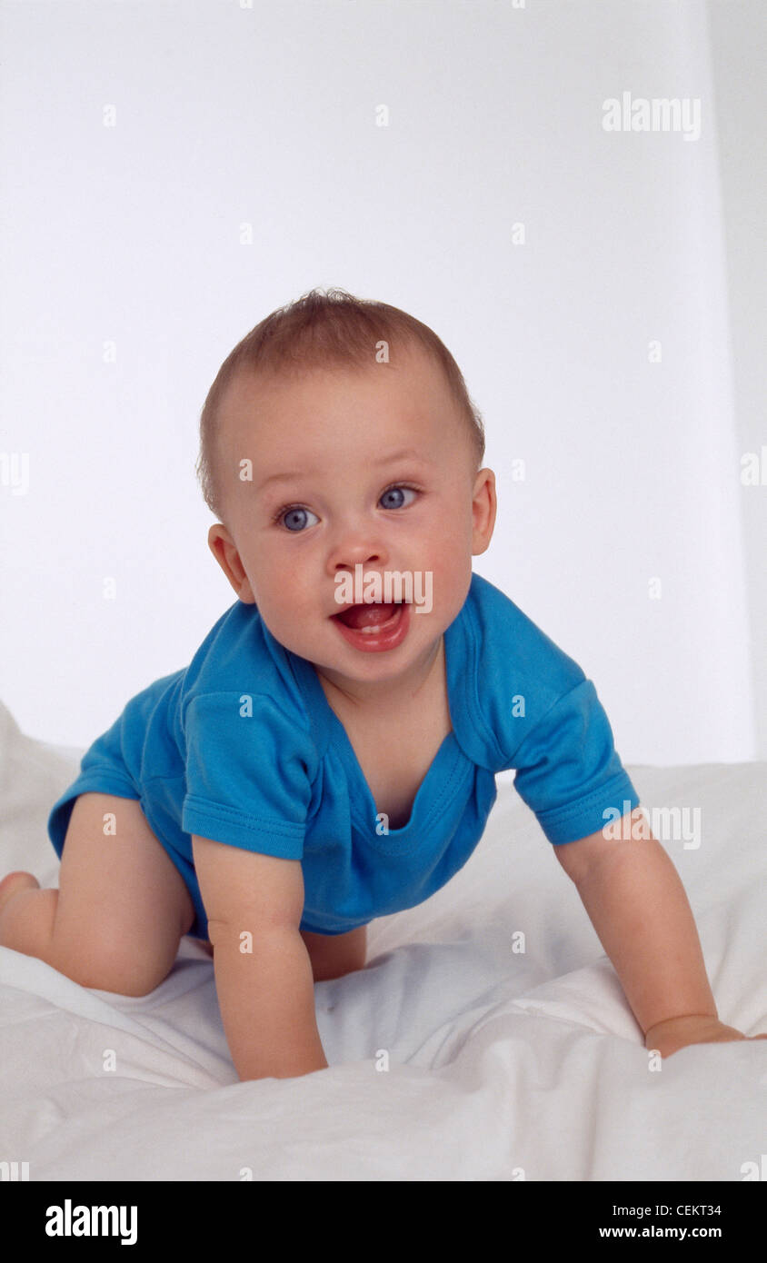 Bébé mâle aux yeux bleus de ramper sur son front sur une couette blanche Banque D'Images
