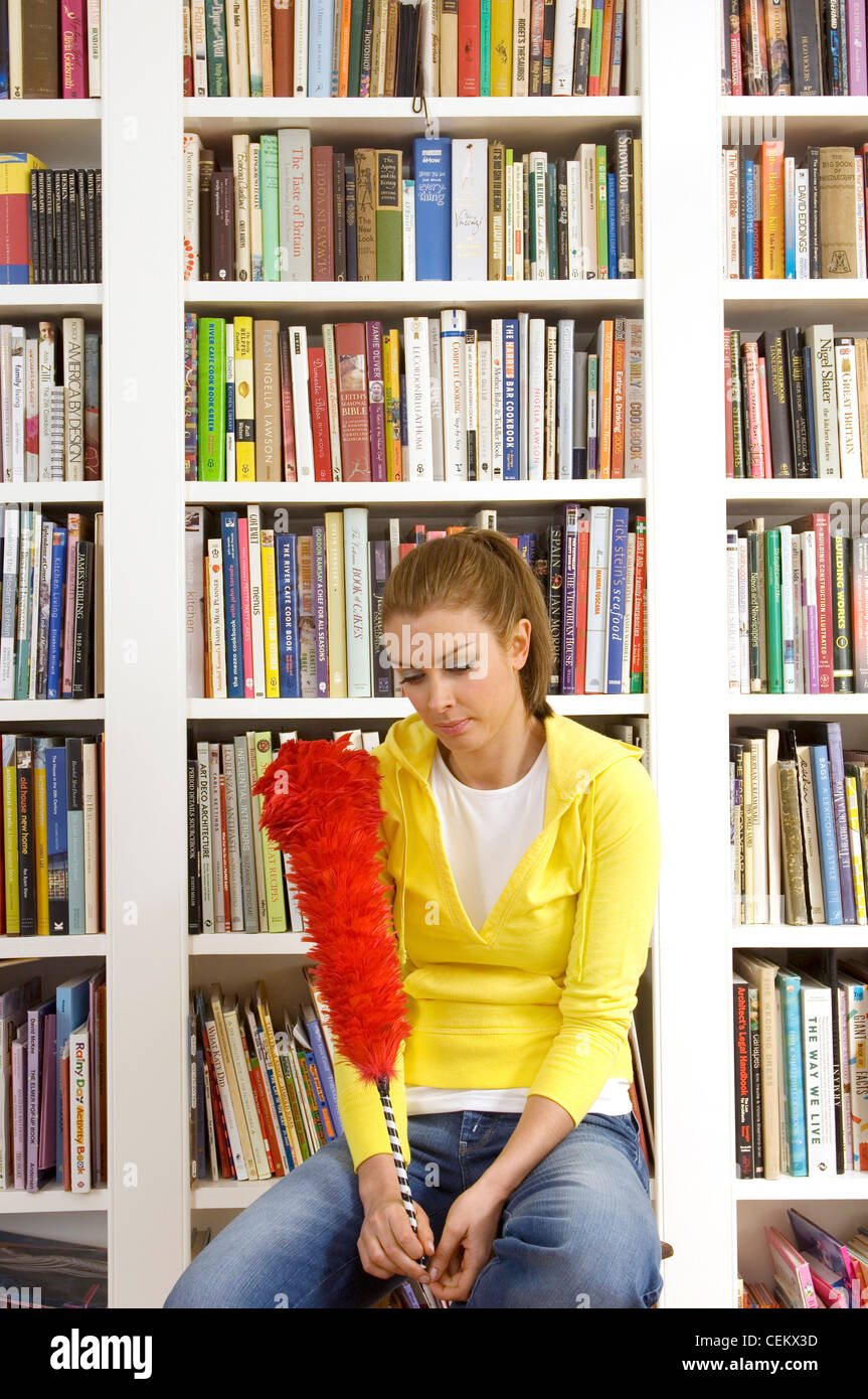 Femme assise sur un escabeau de bibliothèque avec fluffy duster Banque D'Images