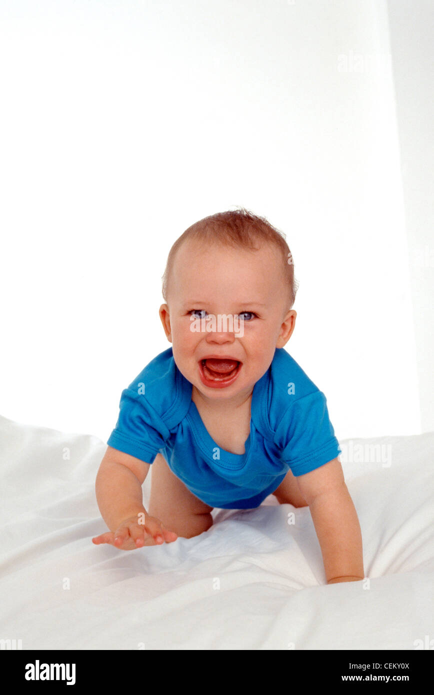 Bébé mâle aux yeux bleus de ramper sur son avant vers l'appareil photo sur une couette blanche sur un lit Banque D'Images