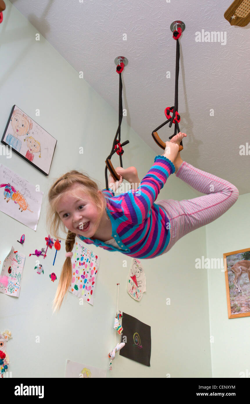 7-ans, fille, accroché sur les anneaux de gymnastique dans sa chambre. Banque D'Images