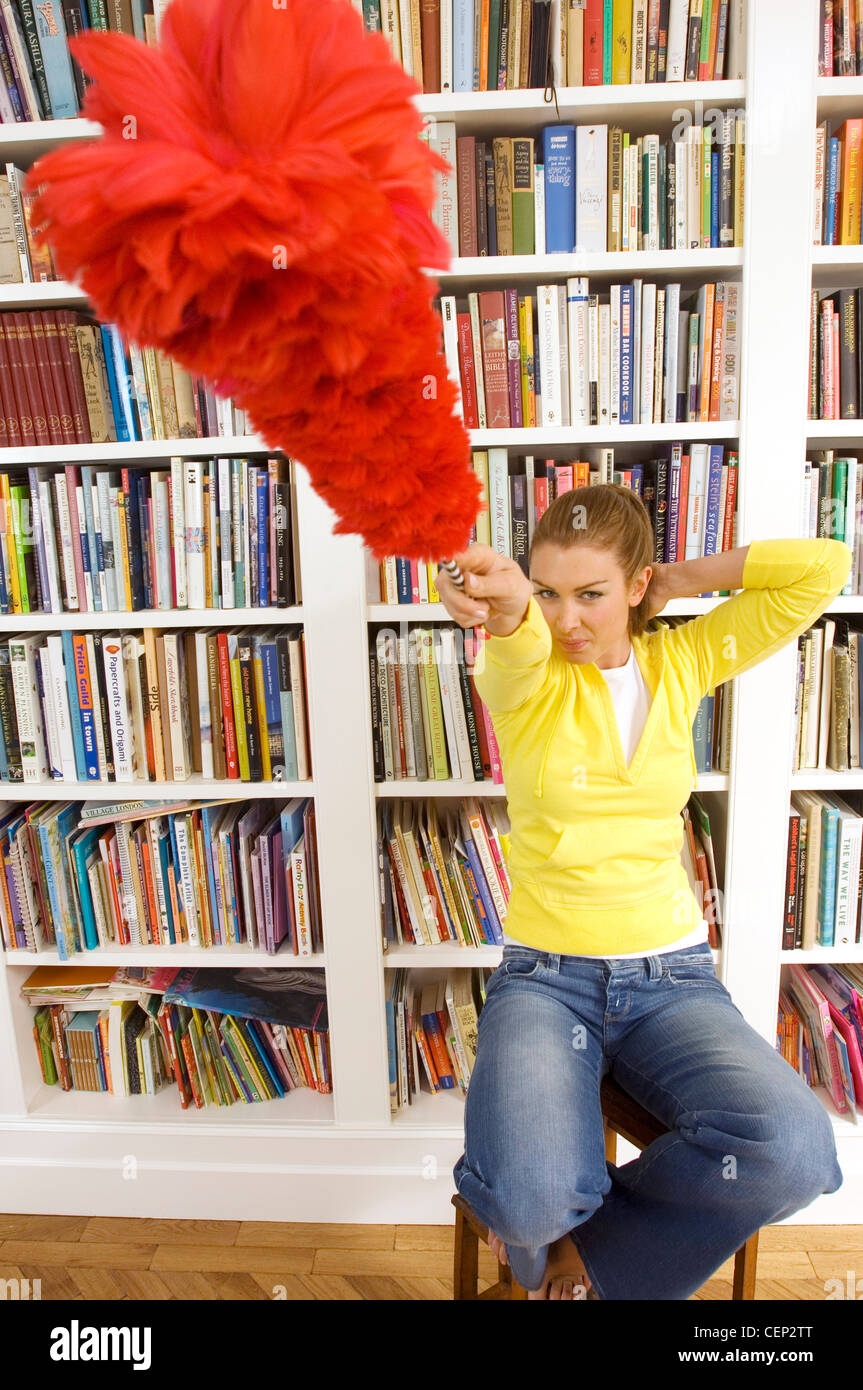 Femme assise sur un escabeau de bibliothèque rouge pointant fluffy duster à l'appareil photo Banque D'Images