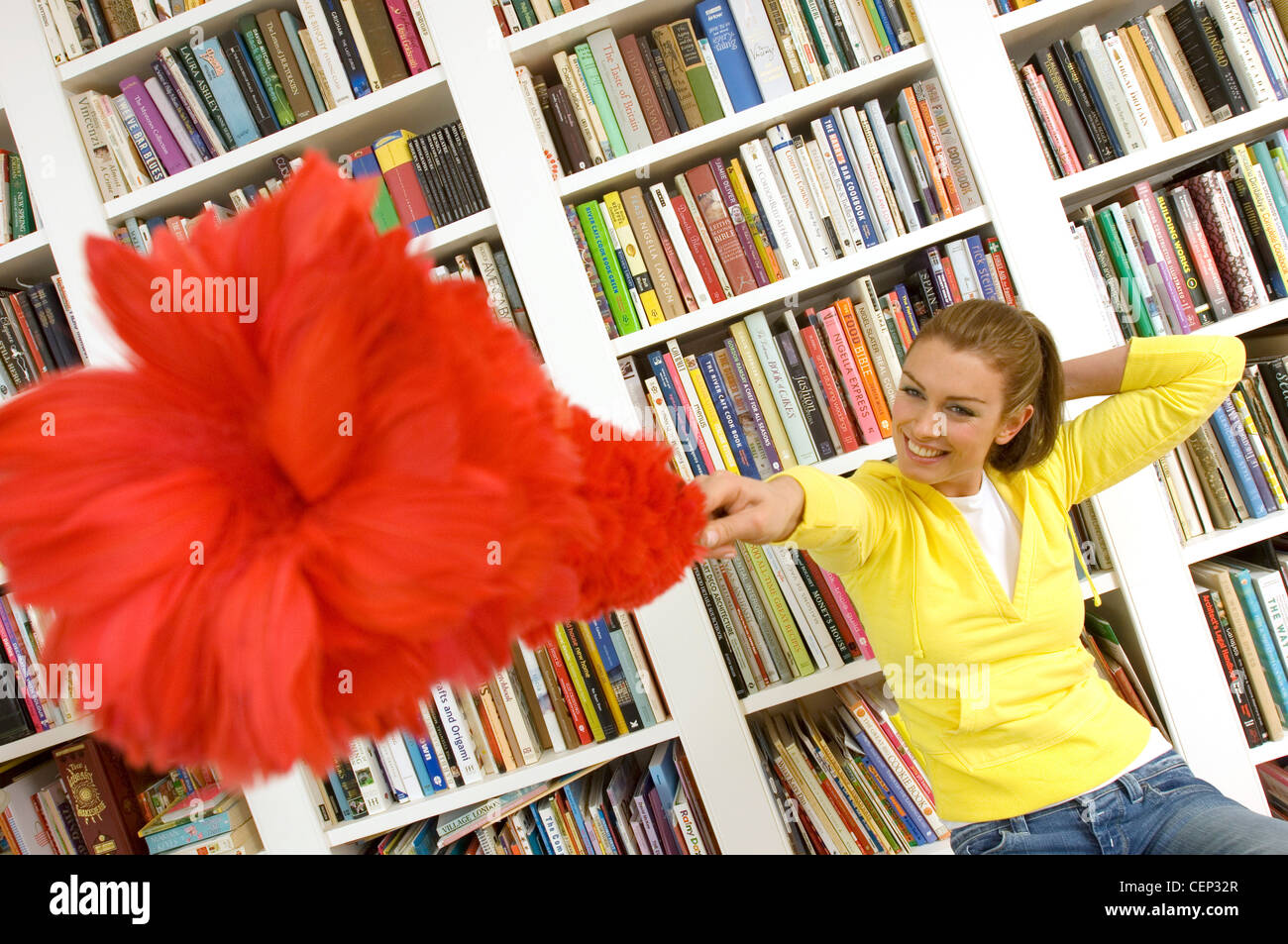 Femme assise sur un escabeau de bibliothèque rouge pointant fluffy duster à l'appareil photo Banque D'Images