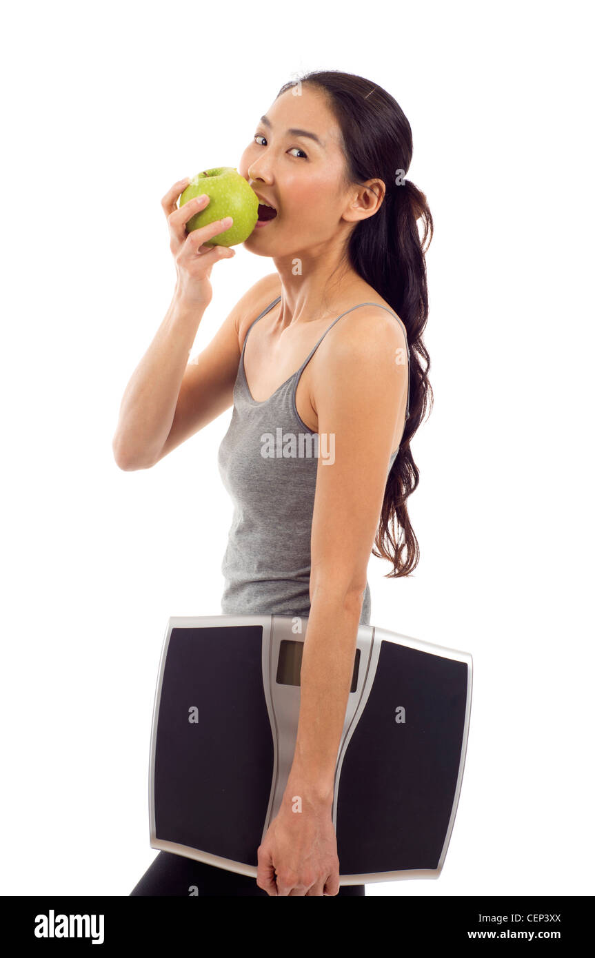 Jeune femme en bonne santé de manger une pomme et de transporter un poids numérique isolé sur fond blanc échelle Banque D'Images