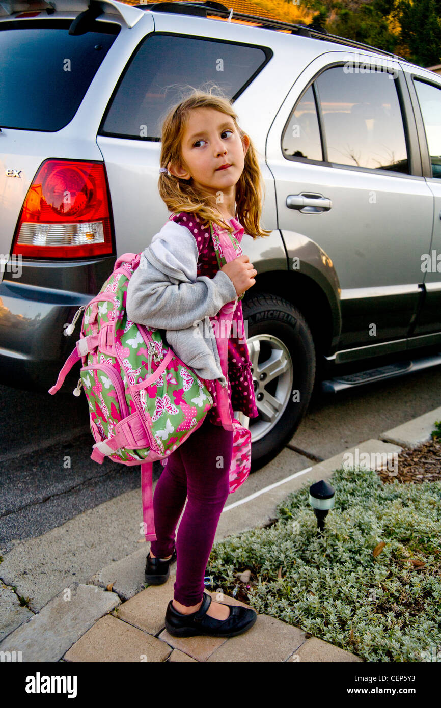 Portant son sac à dos et boîte à lunch, une fillette de 6 ans attend par la voiture pour aller à l'école à San Juan Capistrano CA. Communiqué de modèle Banque D'Images