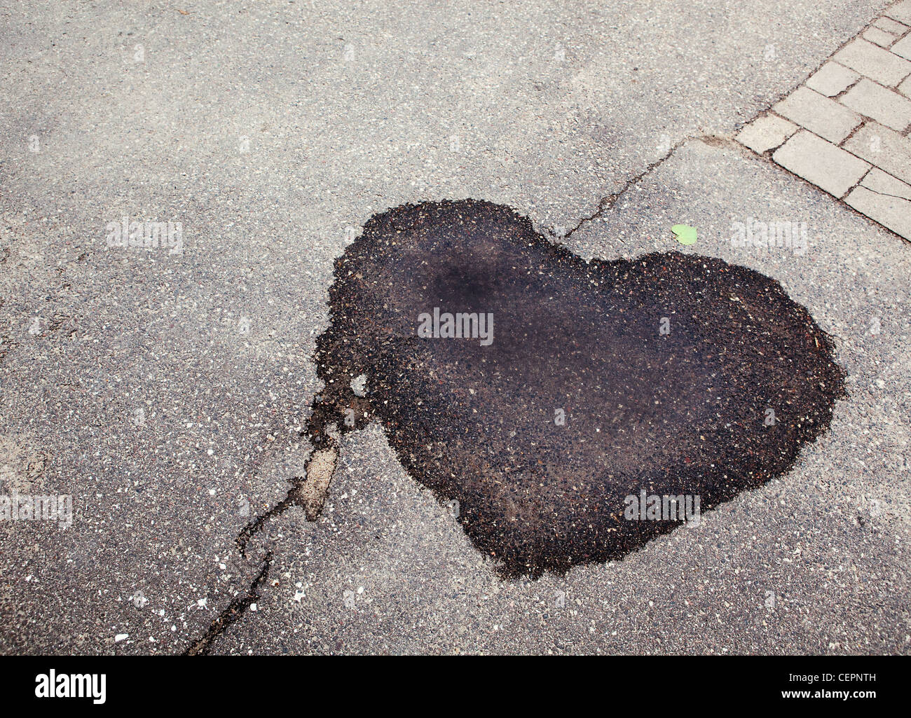 Tache sombre humide de flaque sur le sentier d'asphalte texturé en forme de coeur, abstract background Banque D'Images