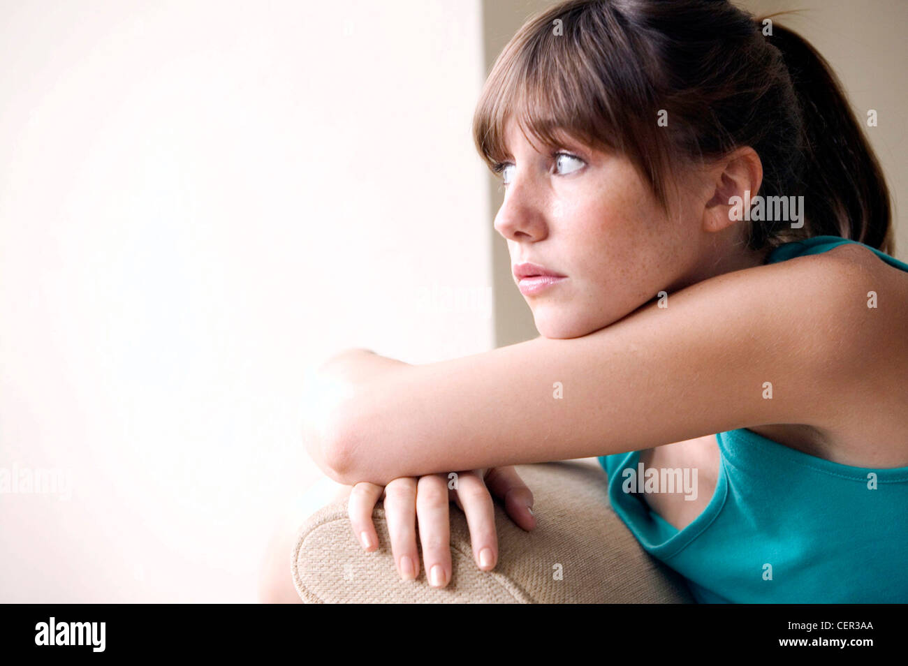 Femme brunette cheveux visage porter gilet vert haut, assis sur un canapé beige, bras croisés sur le bras du fauteuil, bras tête Banque D'Images