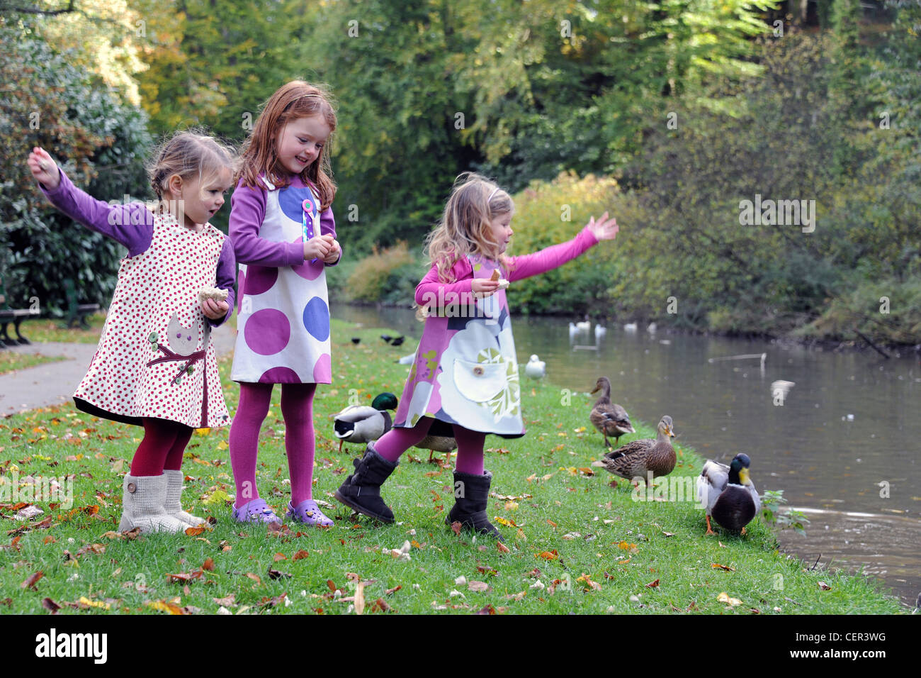 Trois jeunes filles se nourrir du pain pour les canards sur une berge, dans les collines de Hubbard en automne. Banque D'Images