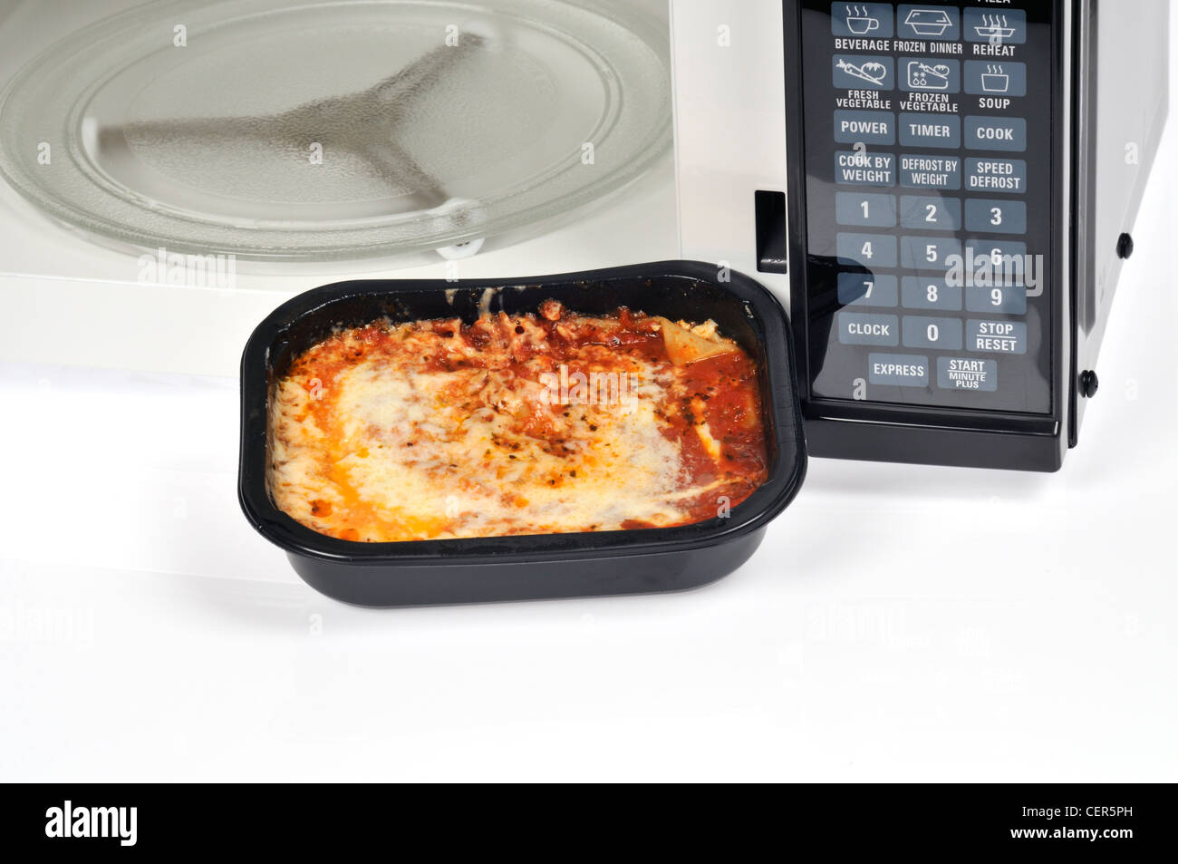 Lasagne cuite dans readymeal bac en plastique noir en face d'un four micro-ondes four avec porte ouverte. Banque D'Images