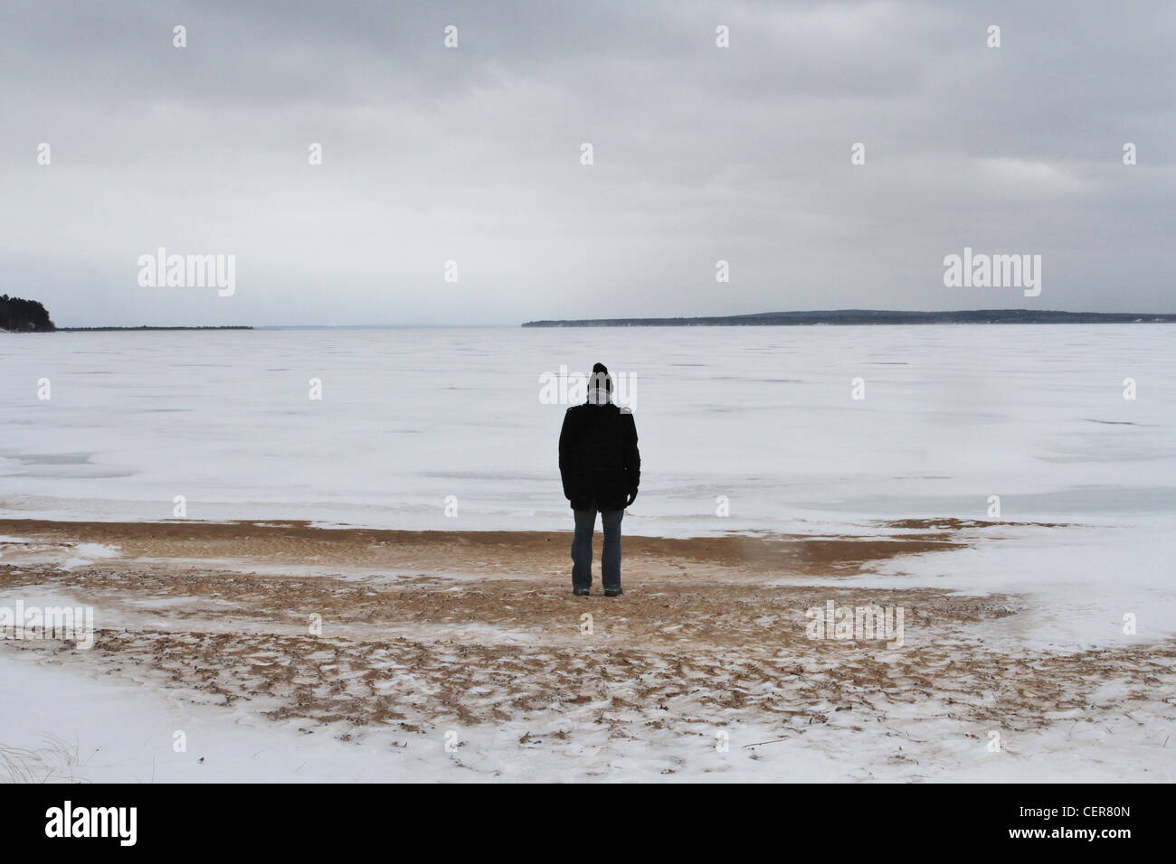 Un homme seul debout sur une plage enneigée et à la recherche au loin dans la distance. Banque D'Images