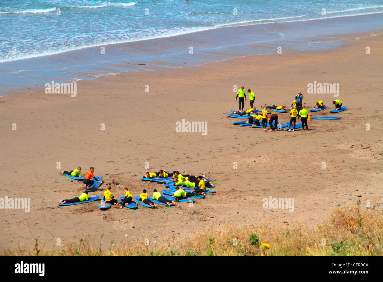 Deux groupes de vacanciers sur une plage de sable fin apprendre à surfer à Widemouth Bay sur la côte nord des Cornouailles près de Bude. Banque D'Images
