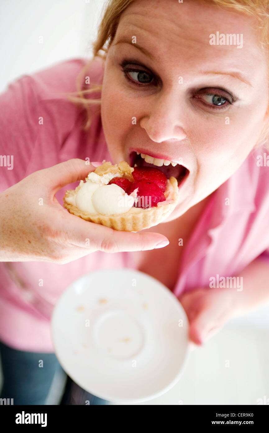 Close up de dessus de cheveux blonds féminine plus importante face off portant la plaque du chandail rose et crème aux fraises un gâteau à la bouche Banque D'Images