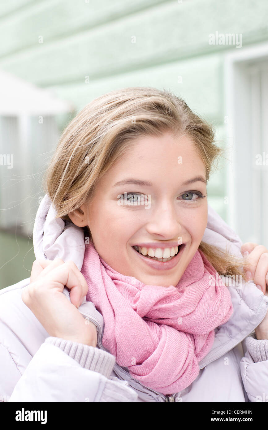 Femme avec des cheveux blond foncé portant mauve pâle manteau rembourré et écharpe rose pâle enroulée autour du cou, les mains sur le collier Banque D'Images