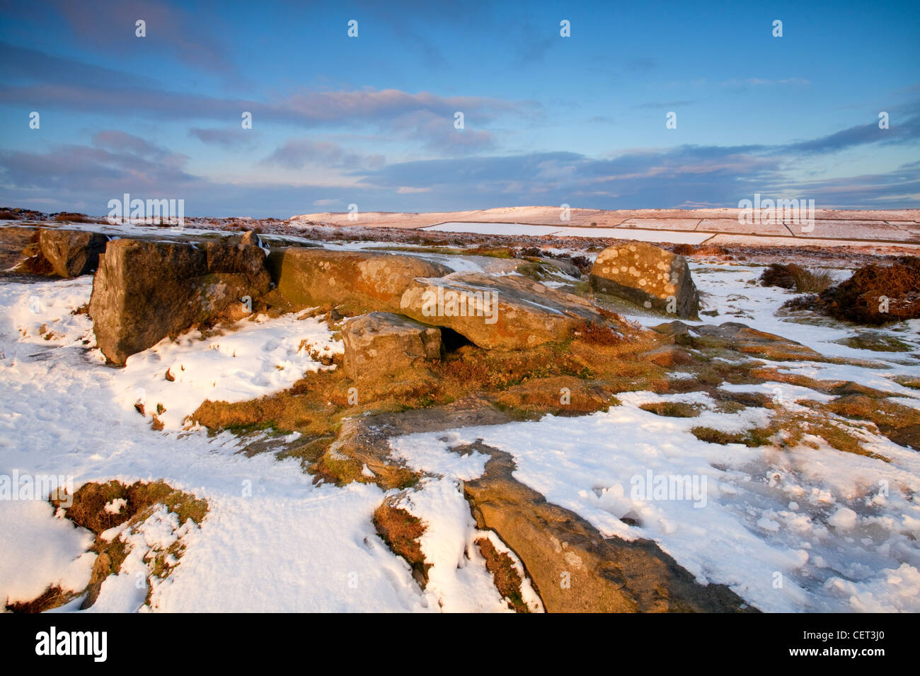 Curbar Edge illuminée par les derniers rayons du soleil couchant dans le parc national de Peak District à la suite d'une chute de neige d'hiver. Banque D'Images