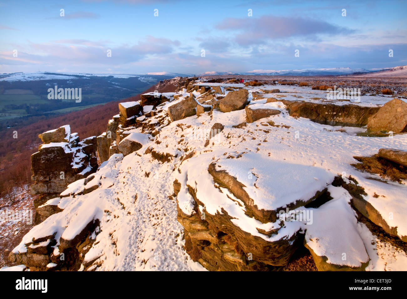 Curbar Edge illuminée par les derniers rayons du soleil couchant dans le parc national de Peak District à la suite d'une chute de neige d'hiver. Banque D'Images