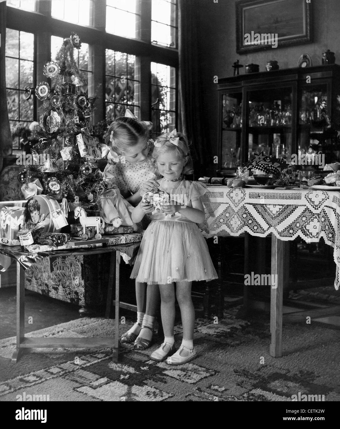 Deux filles attacher les cheveux juste porter des rubans robe debout à côté à la table dans la salle de séjour, un holding Christmas Banque D'Images