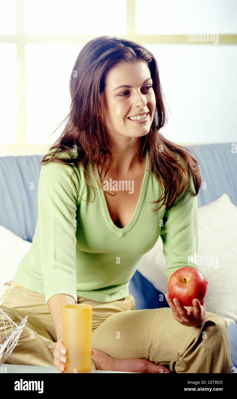 Femme brunette wearing long cheveux vert Pull col en v et un pantalon beige assis sur canapé une jambe dans l'autre, Banque D'Images