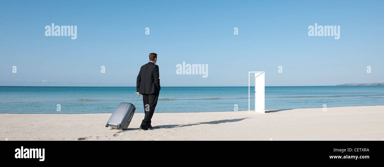 Businessman pulling suitcase sur plage, à marcher vers la porte à moitié ouverte Banque D'Images