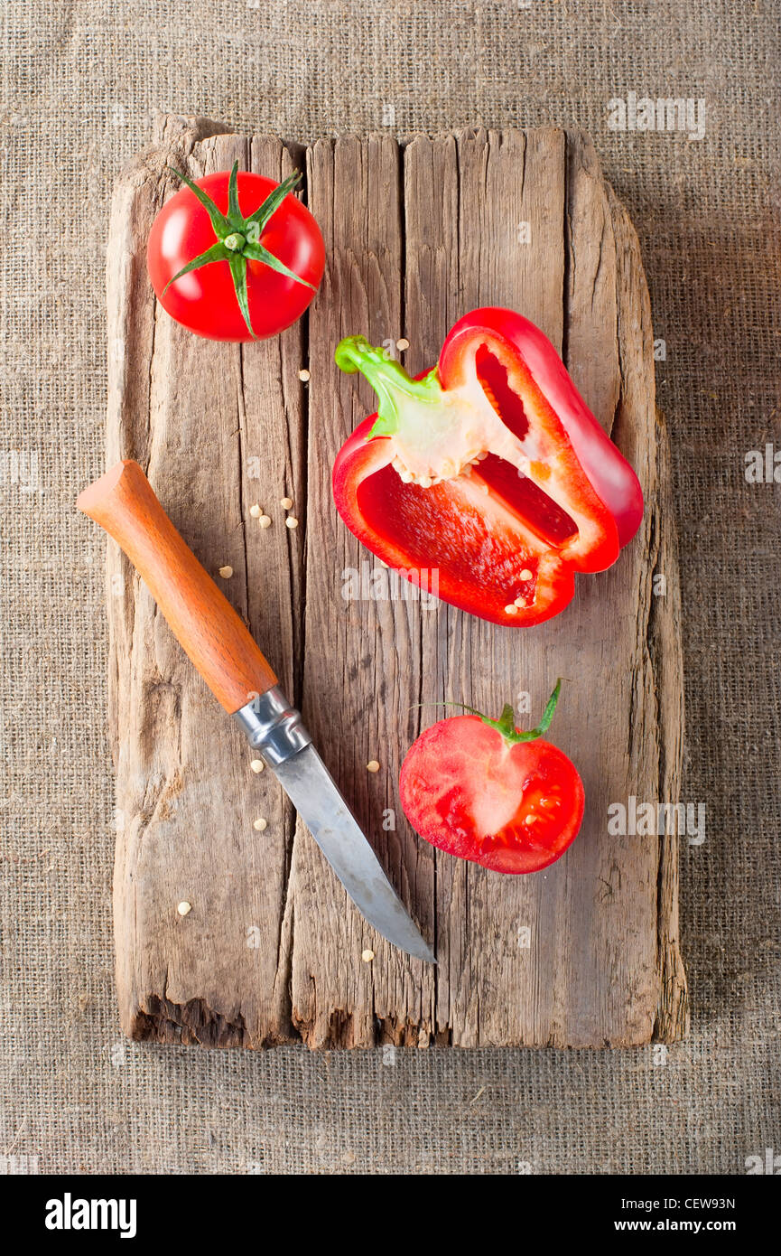 Tomate fraîche, paprika, couteau en acier et planche à découper en bois vintage sur toile cirée Banque D'Images