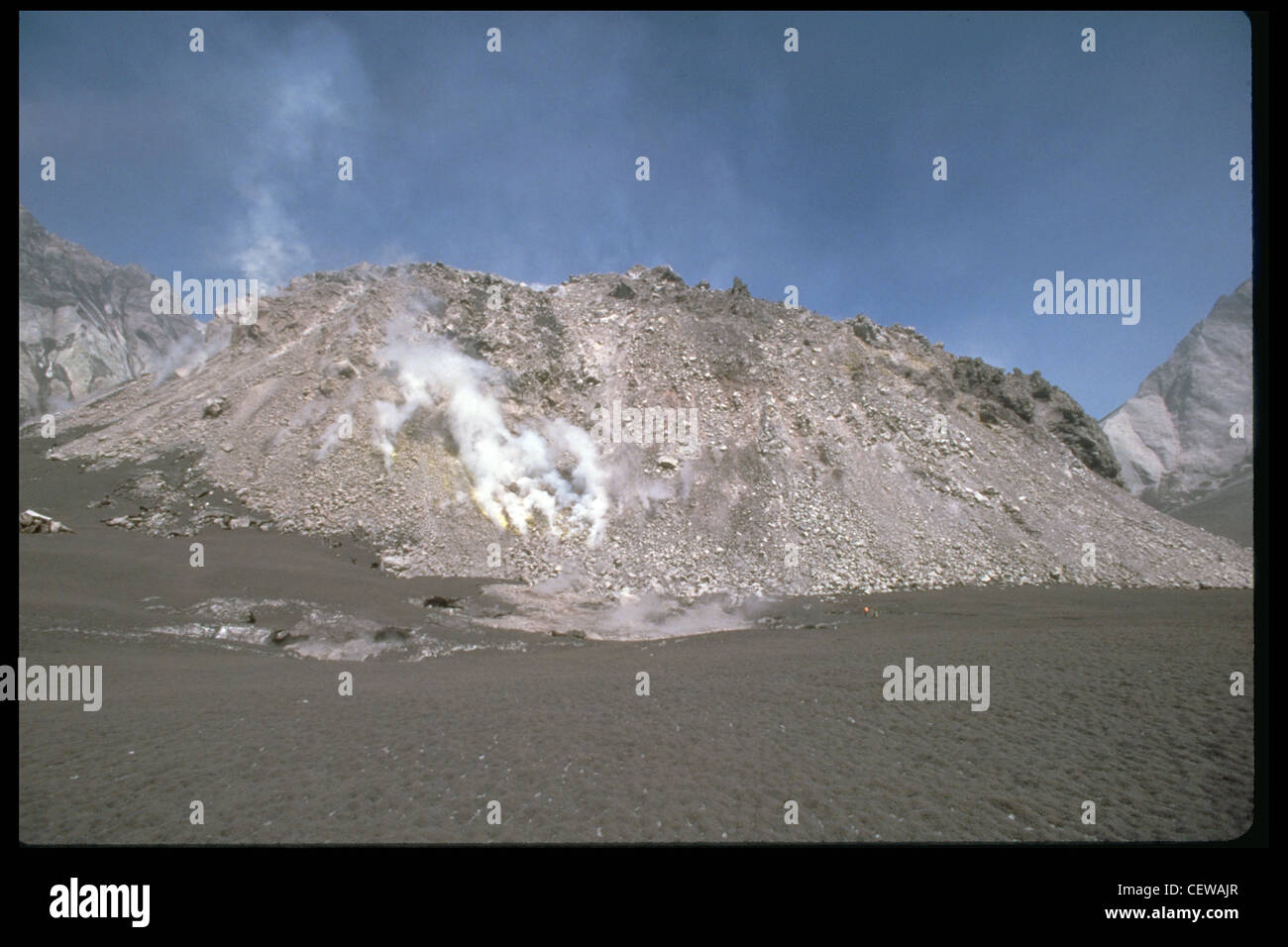 Deux géologues de la Commission géologique des États-Unis (un en orange, au milieu à droite, près de la base du dôme) sont nains par le dôme. Les géologues se tiennent sur la neige, mudède depuis les récents chutes. En 1987, le dôme avait remplacé seulement trois pour cent du volume enlevé par l'éruption du 18 mai 1980. Si ce taux de croissance avait continué, il aurait fallu plus de 200 ans pour reconstruire le mont St. Helens à sa taille d'avant 1980. Au lieu de cela, le mont St. Helens est entré dans une période tranquille qui a continué jusqu'en 2004. Banque D'Images
