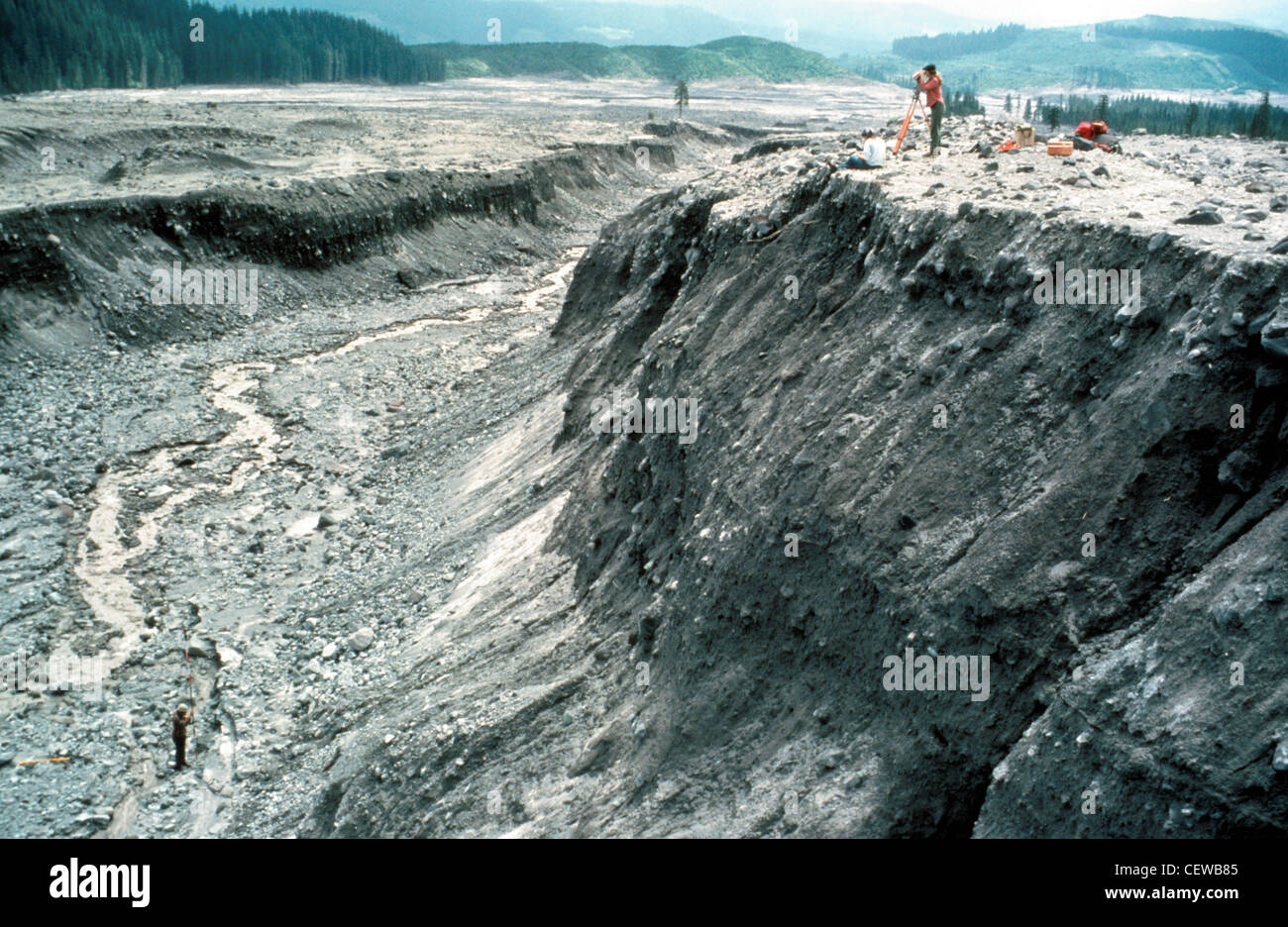 Les hydrologues de la U.S. Geological Survey ont mesuré les changements dans l'érosion le long des canaux du cours d'eau touchés par l'éruption du 18 mai 1980. Ces mesures ont été utilisées pour étudier les processus d'érosion et pour estimer la gravité du problème de sédimentation. La vue ici se trouve le long du bassin versant de la rivière Muddy, à environ 1.5 kilomètres au sud-est de la base du volcan. La personne de la tige (en bas à gauche) et les personnes de l'instrument (en haut à droite) donnent la balance. Banque D'Images