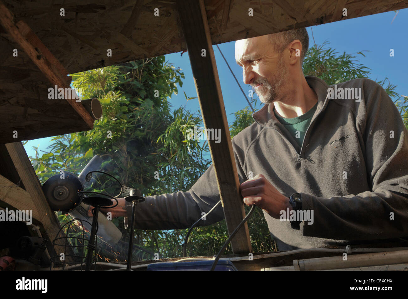 Un homme en train de réparer le toit de son hangar à l'aide d'un outil électrique Banque D'Images