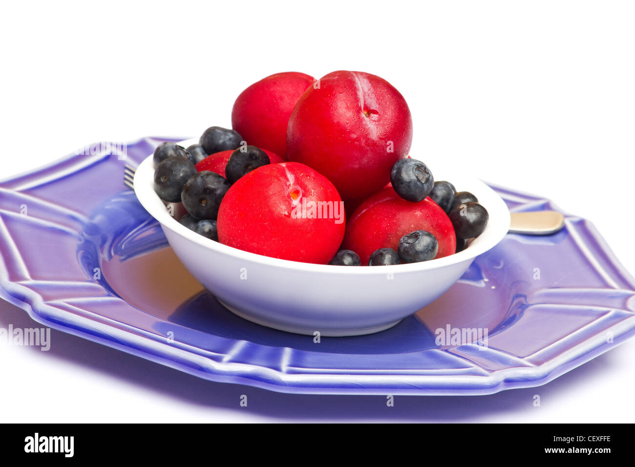 Les prunes fraîches et les bleuets dans un bol blanc sur fond blanc Banque D'Images
