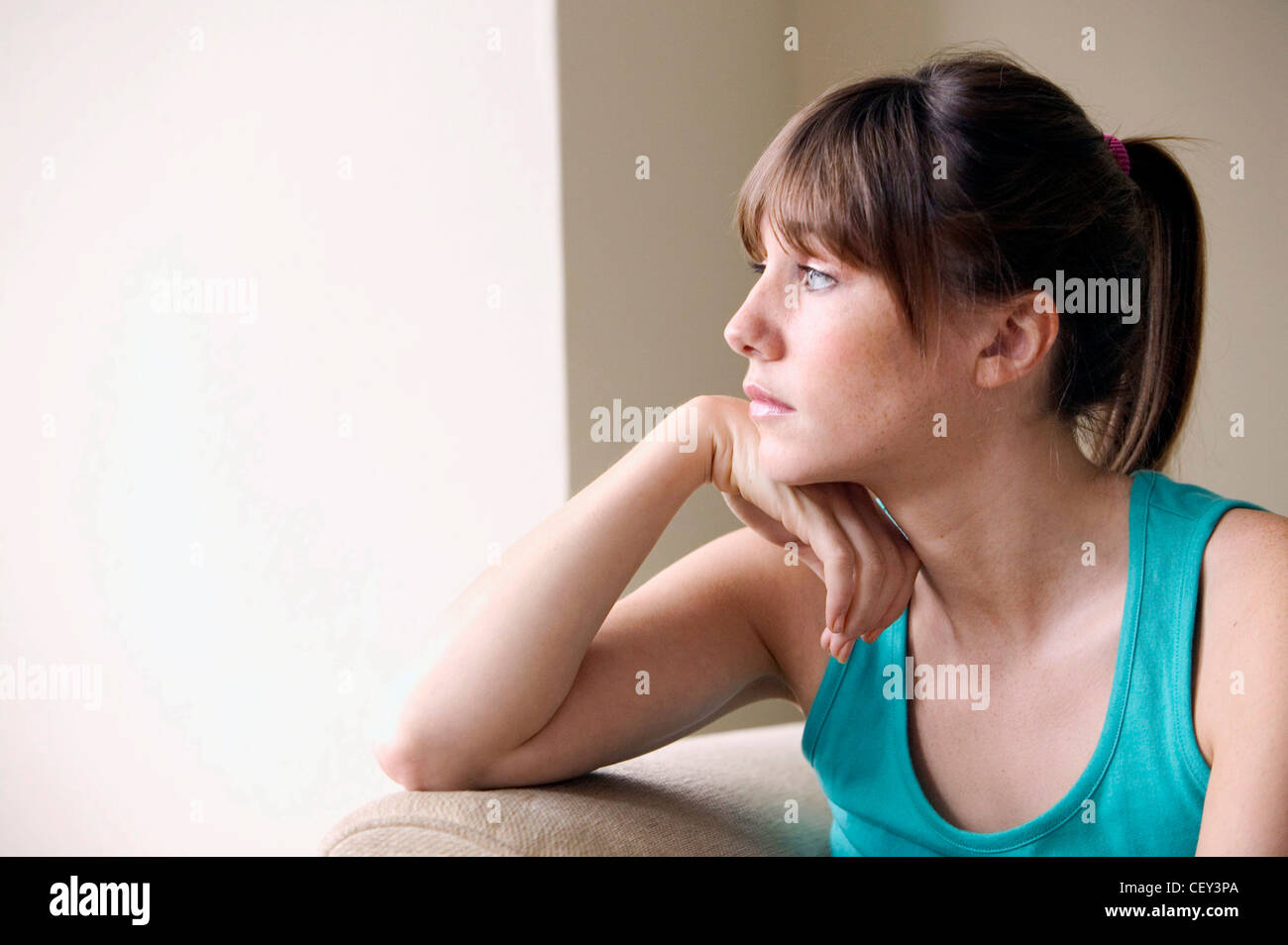 Femme brunette cheveux visage porter gilet vert haut, assis sur le canapé beige tête reposant sur la main, à côté d'OF Banque D'Images