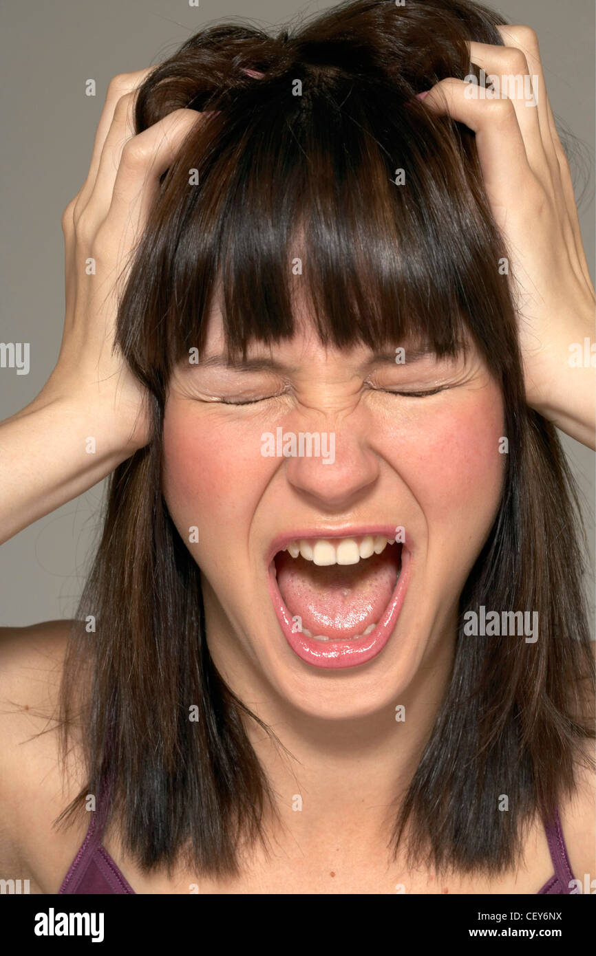 Tête de femme brune cheveux frangée, hurlant de frustration, fermé les yeux et serré les deux mains saisissant son Gris de cheveux Banque D'Images