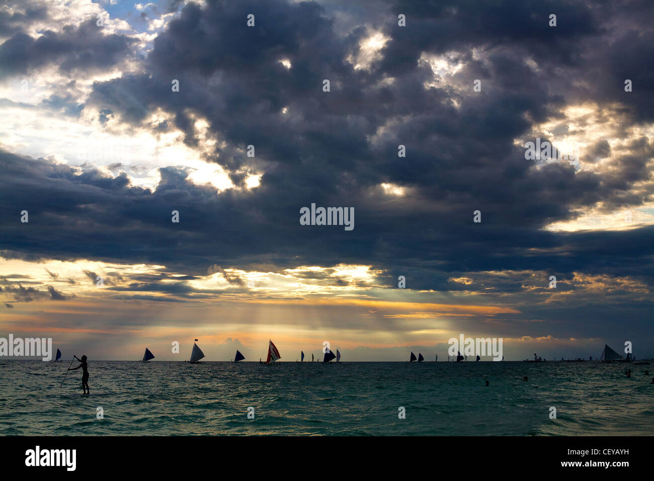 Coucher du soleil transperce les nuages et les lumières de l'horizon à Boracay, Province d'Aklan, Philippines. Banque D'Images