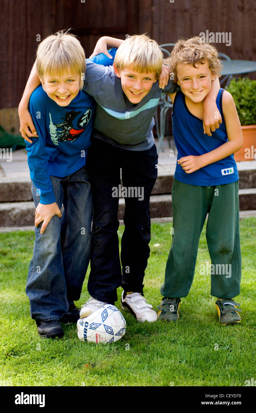 Trois enfants mâles avec leurs bras autour des épaules de chacun avec le football Banque D'Images