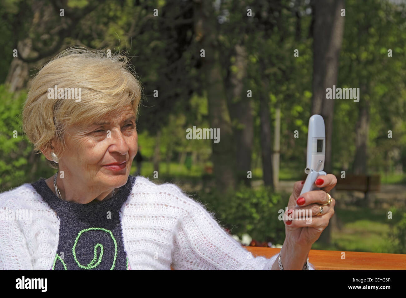 Senior woman en utilisant un téléphone mobile pour prendre des photos dans un parc. Banque D'Images