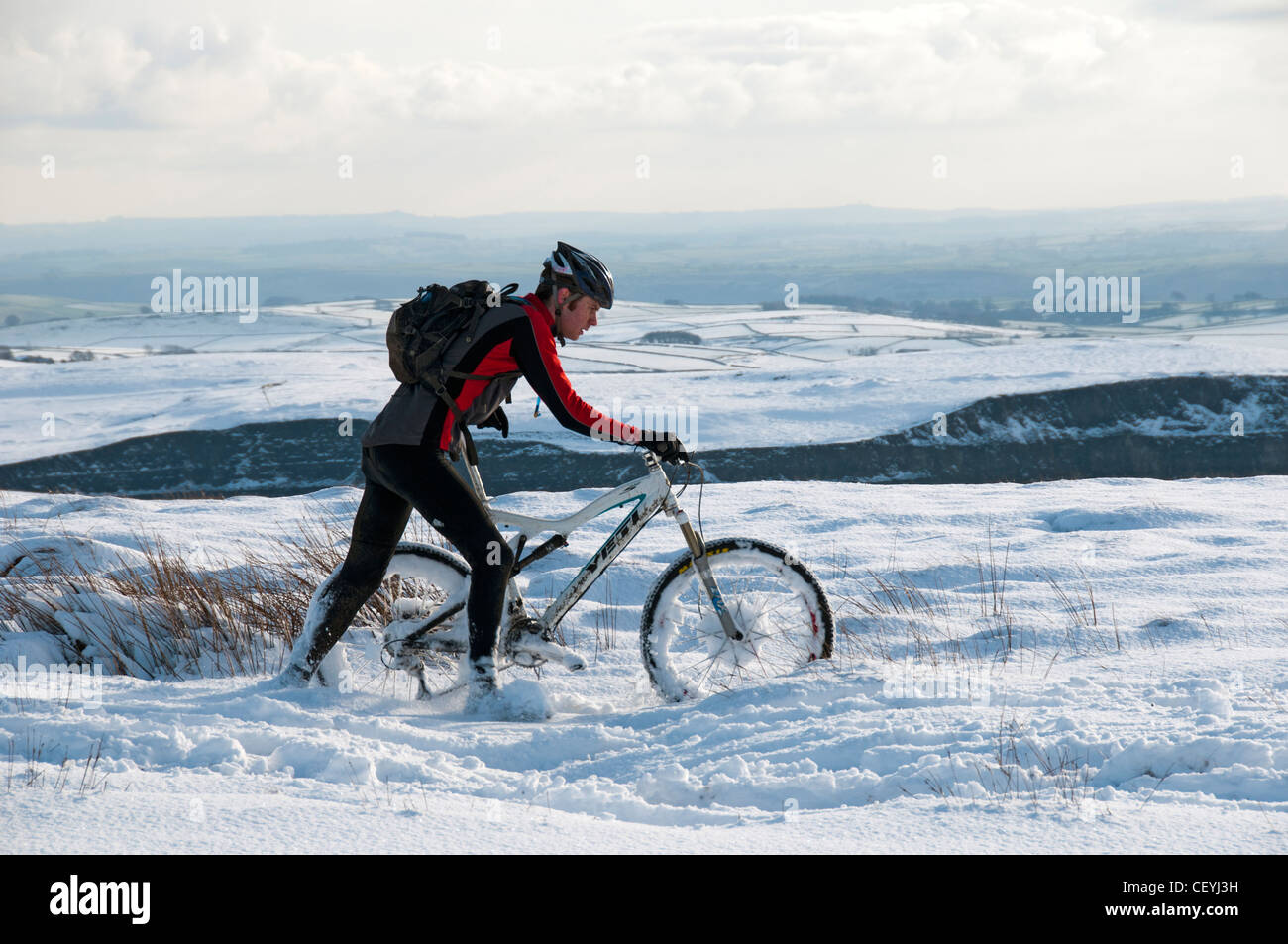 Un vélo de montagne pousse son vélo dans la neige épaisse sur Rushup Edge, près de Castleton, Derbyshire, Angleterre, RU Banque D'Images