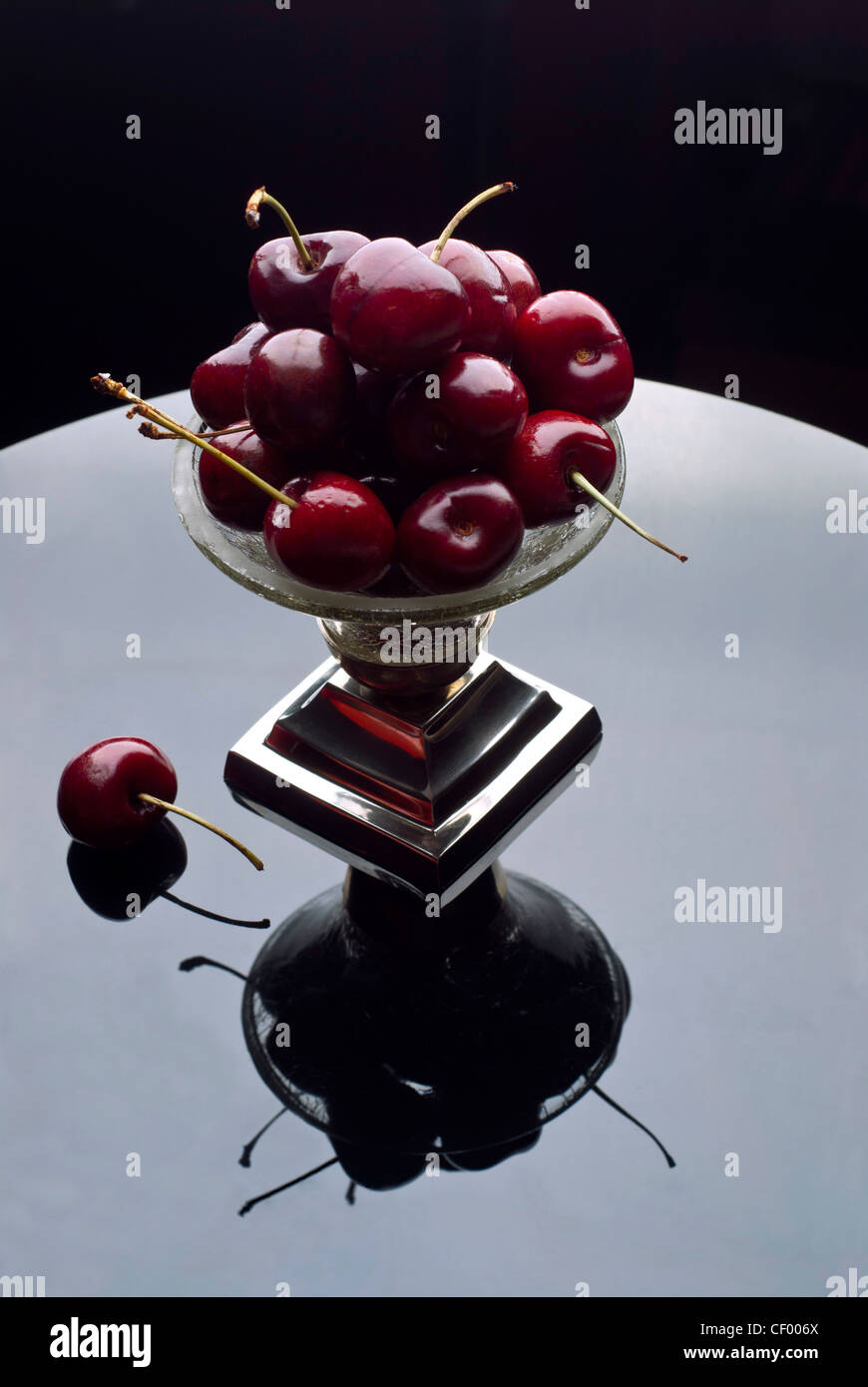 Cerise rouge entassés dans un bol en argent cristal reflète dans une surface réfléchissante Banque D'Images