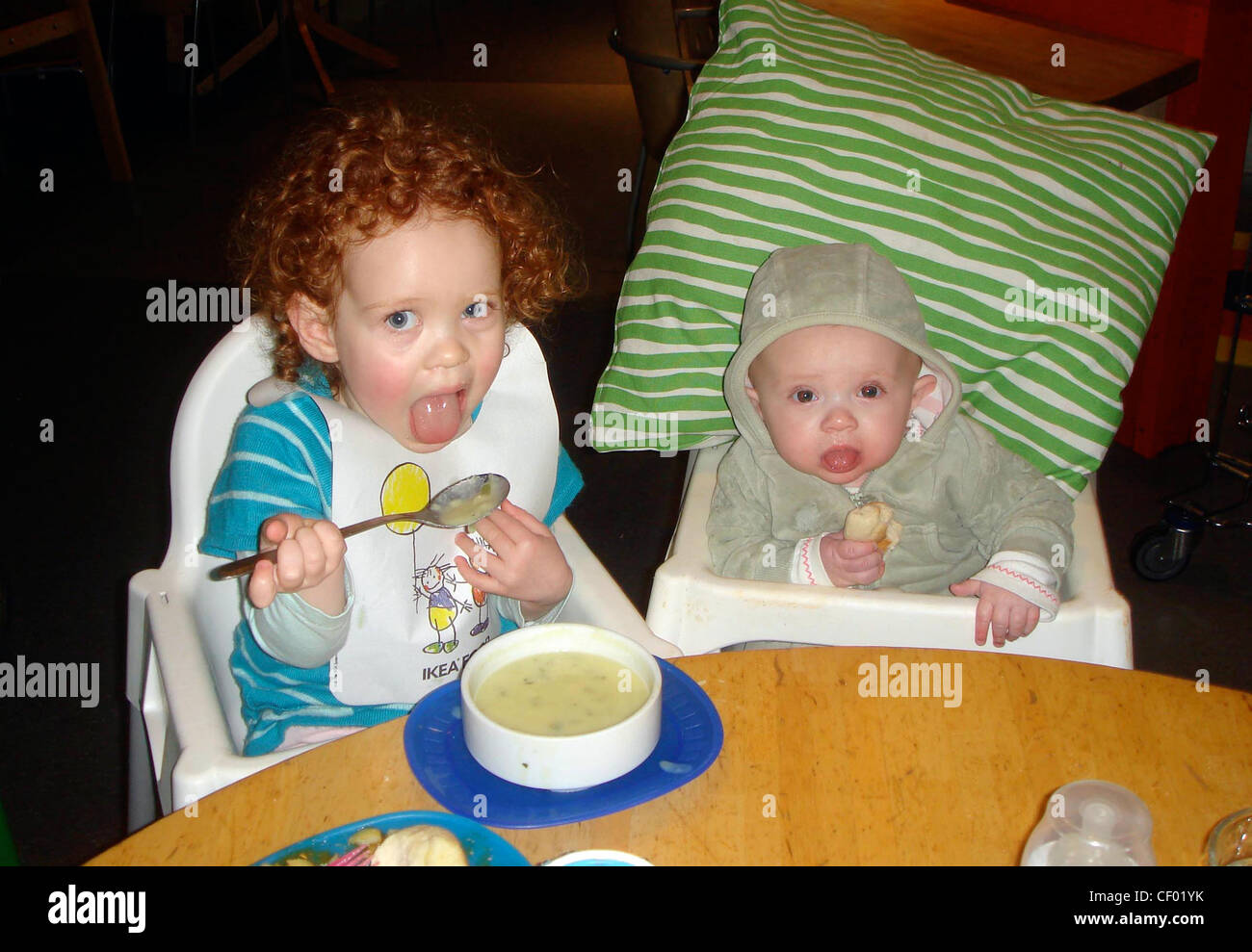 Enfant De Sexe Feminin Les Cheveux Rouge Boucles Portant Robe Tricote Bleu Et Ikea Bib Et Femelle Bebe En Haut A Capuchon Vert Assise En Blanc Photo Stock Alamy