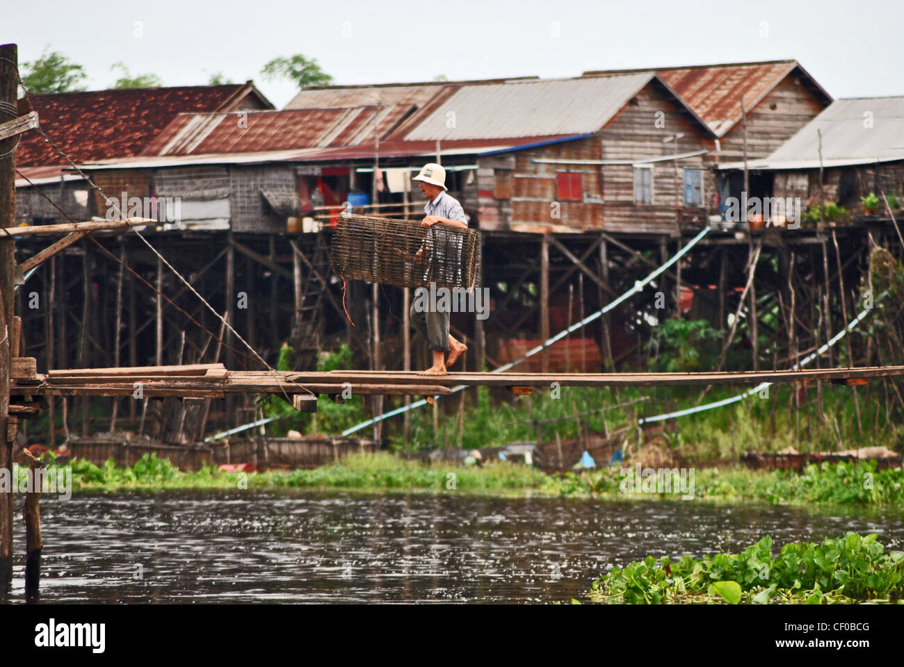 L'homme de traverser un pont avec un piège à poissons à Kompong Khleang village, Cambodge Banque D'Images