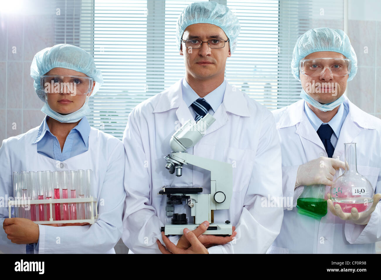 Trois scientifiques sérieux maintenant l'équipement de laboratoire et looking at camera Banque D'Images