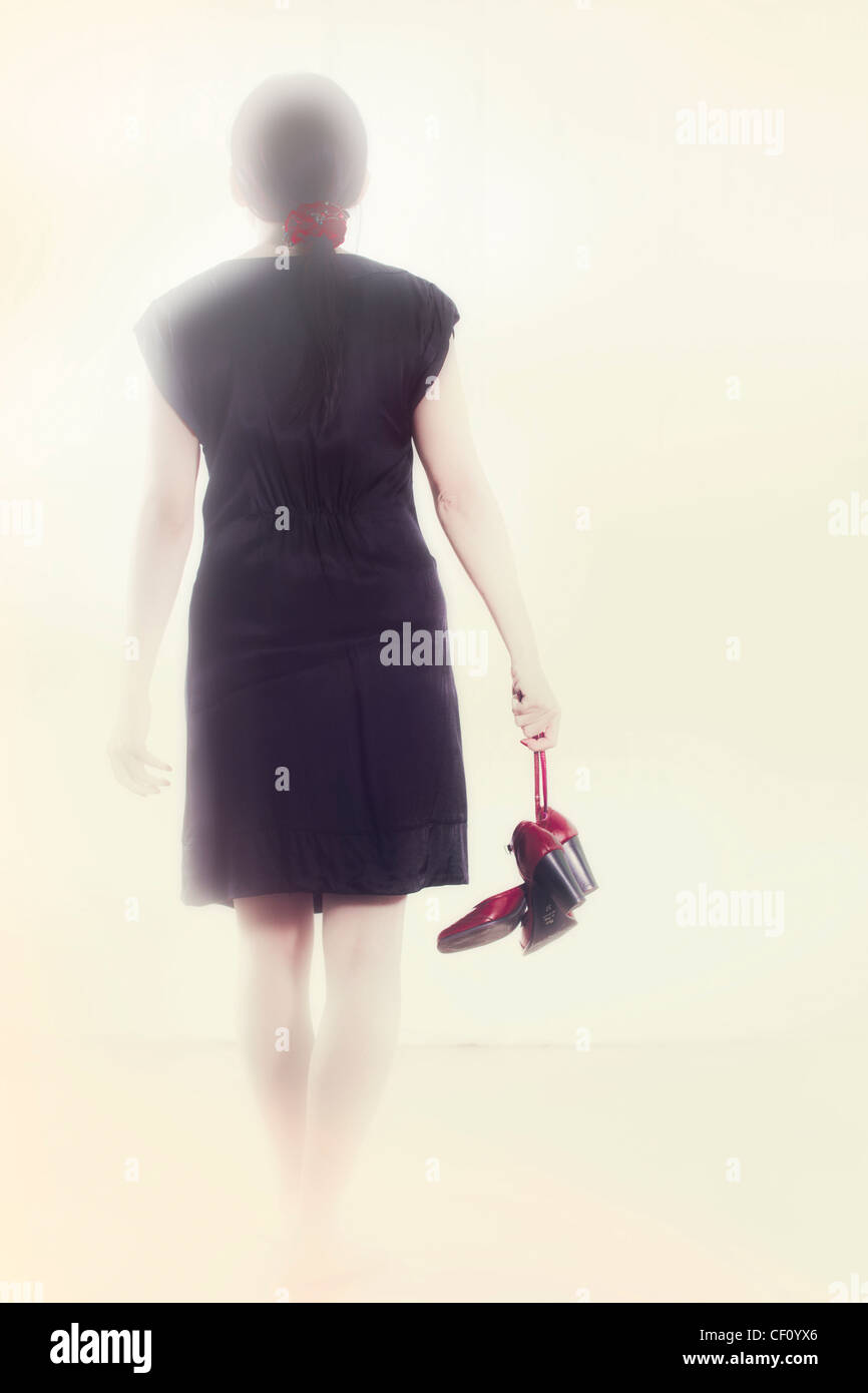 Femme dans une robe noire va avec chaussures rouges en main dans la lumière Banque D'Images