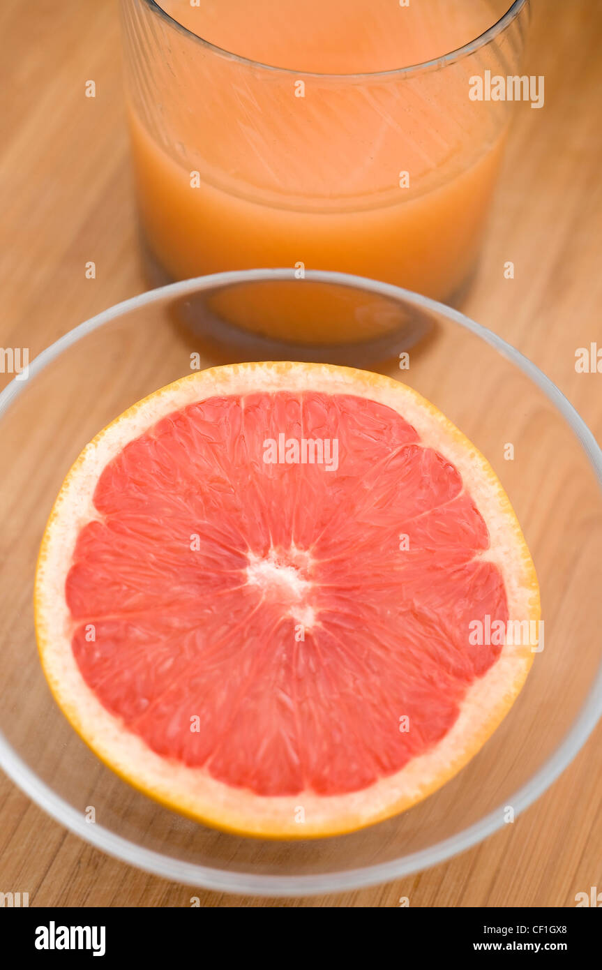 Une moitié du pamplemousse dans un bol en verre clair et un verre de jus Banque D'Images