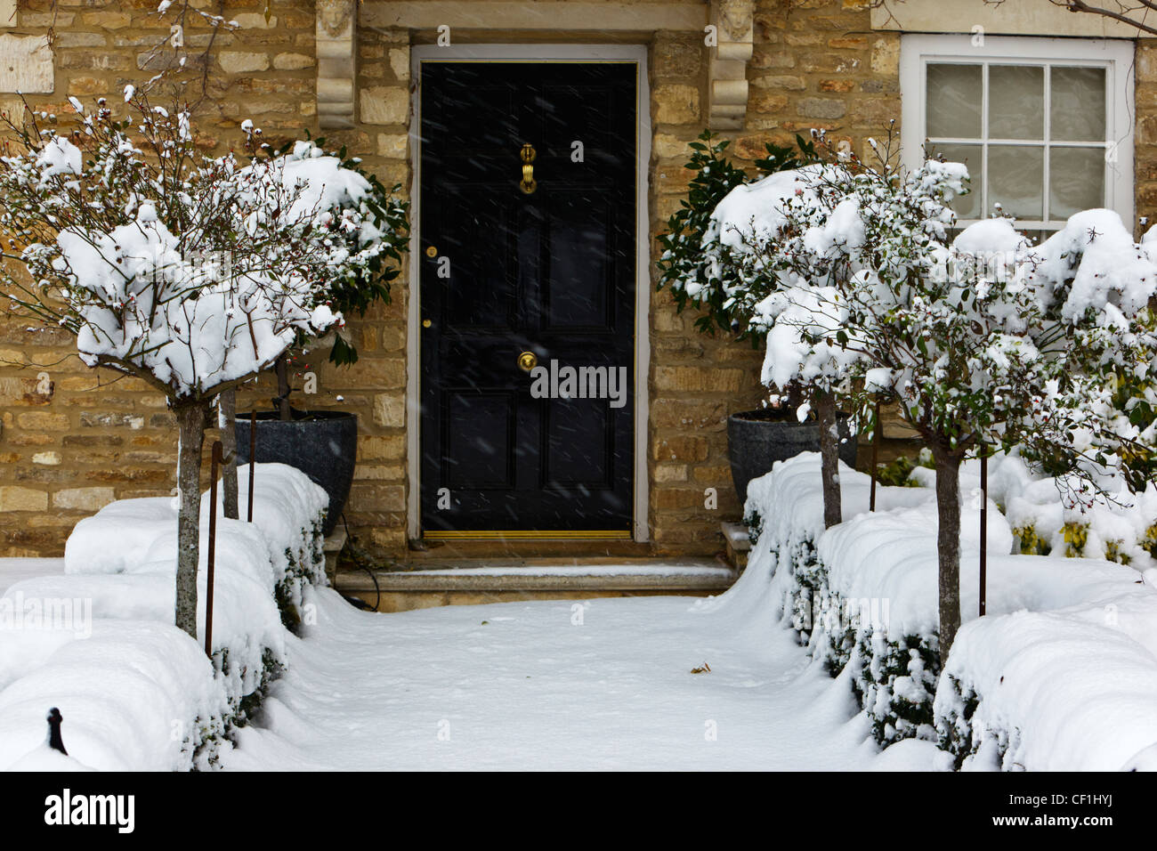 Un chemin couvert de neige menant à une porte avant de noir une maison construite en pierre dans la région des Cotswolds. Banque D'Images