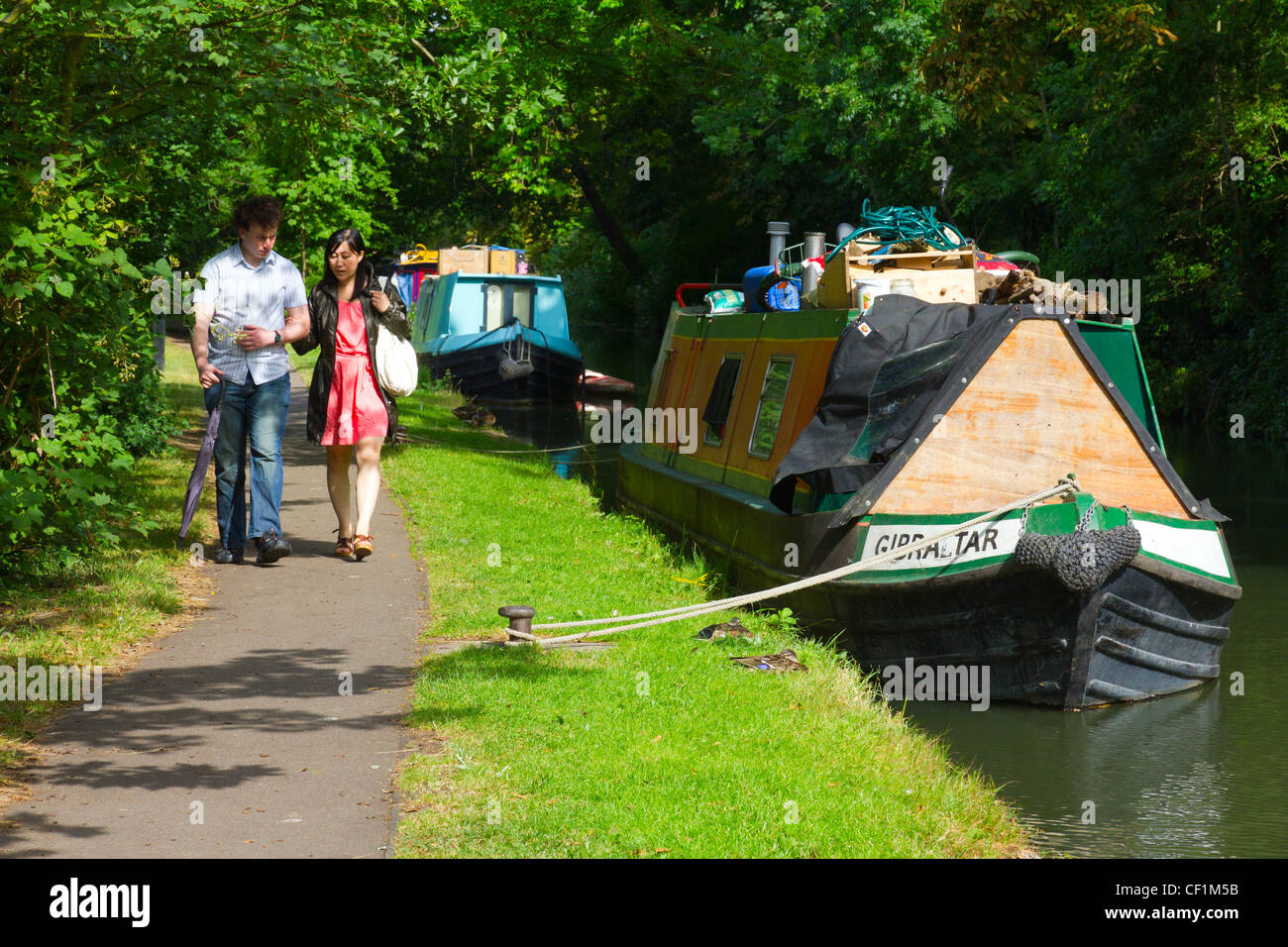 Un couple en train de marcher le long du chemin du canal péniches amarrés sur le passé du canal d'Oxford. Banque D'Images