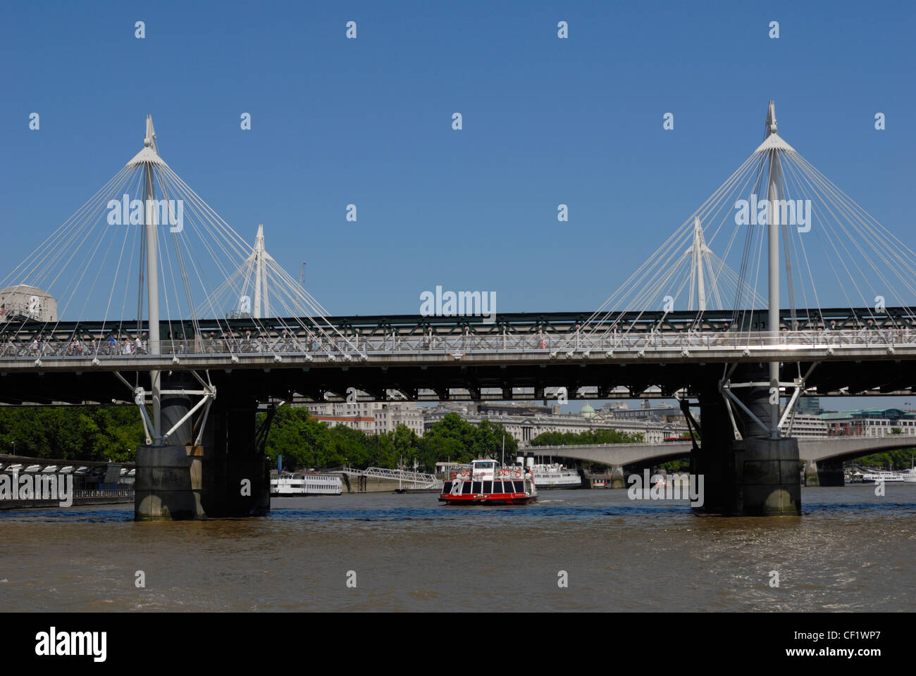 Un bateau se déplaçant le long de la Tamise sous le Hungerford Bridge (Pont de Charing Cross). Banque D'Images