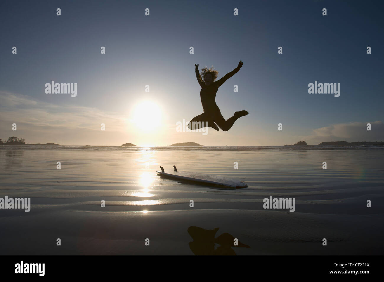 Silhouette de femme Surfer sauter de joie ; Chesterman Beach Tofino Vancouver Island British Columbia Canada Banque D'Images