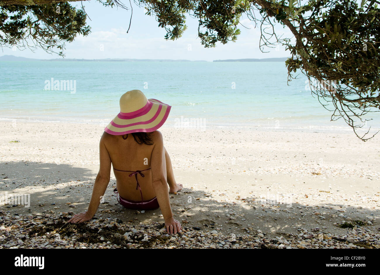 Une femme assise sur la plage portant un chapeau à large chapeau d'été en admirant la vue Banque D'Images